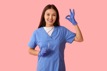 Young female dentist with floss toothpick showing OK on pink background