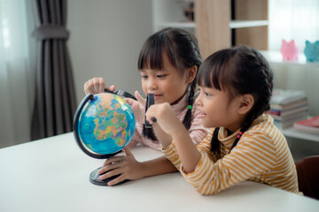 Two Asian little girl is learning the globe model, concept of save the world and learn through play activity for kid education at home.