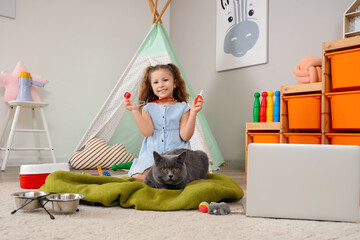 Cute little girl with British cat, laptop and first aid kit at home