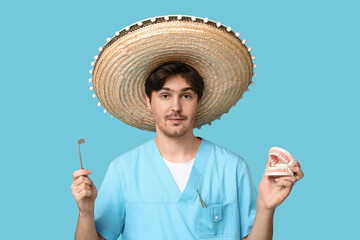 Fototapeta premium Young male dentist with sombrero, dental mirror and jaw model on blue background
