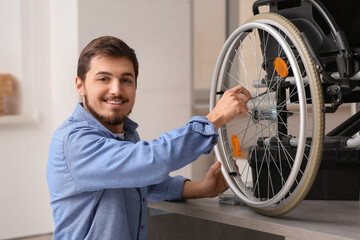 Young man with wrench repairing wheelchair on table at home