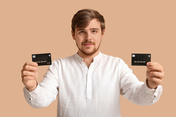 Young man with credit cards on beige background