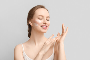 Young woman with cream on grey background