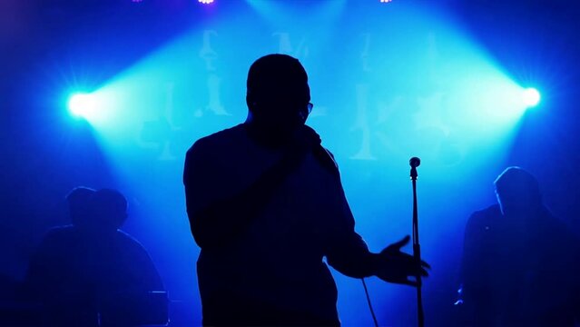 Silhouette of rap singer performing on stage. Bright blue background with hip hop artist performing on concert in night club