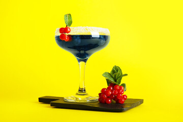 Glass of tasty cocktail with blueberry and cranberry on yellow background