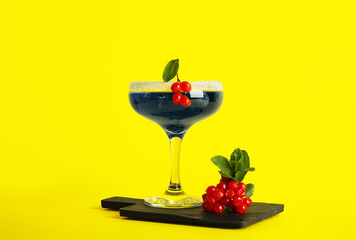 Glass of tasty cocktail with blueberry and cranberry on yellow background