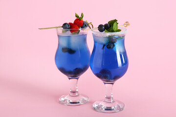 Glasses of tasty cocktail with blueberry and strawberry on pink background