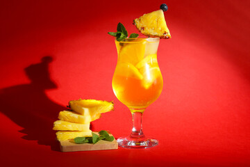 Glass of tasty cocktail with pineapple and orange on red background