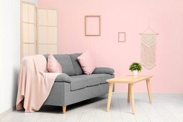 Cozy sofa with cushions, plaid and coffee table with plant in living room