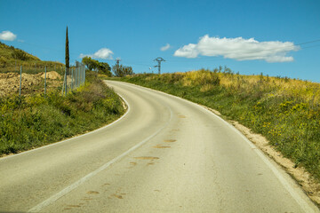 The asphalt road goes into a curve running among fields and meadows on a sunny summer day. Blue sky with white curly clouds. Good weather. Travel.