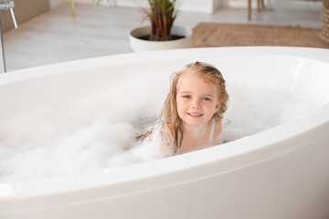 Cute little girl with foam taking bath in bathroom