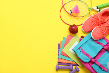 Dumbbells, badminton rackets, shuttlecock, sneakers, apple and different stationery on yellow background