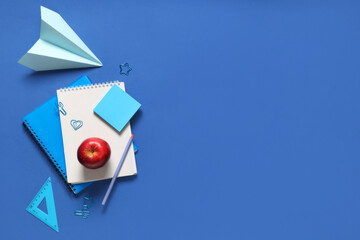 Tasty apple, paper airplane and different school stationery on blue background