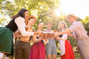 Young people in traditional German clothes with beer and sausages celebrating Octoberfest outdoors