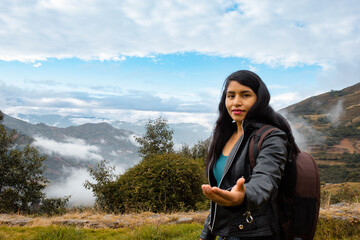 Naklejka premium Hermosa foto de una feliz viajera hispana con una mochila en la cima de montañas verdes.cielo dia.Concepto de viaje turismo.