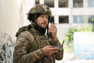 Military mission. Soldier in uniform with drone controller and radio transmitter near abandoned building outdoors