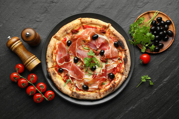 Tasty pizza with cured ham, olives, tomatoes and parsley on black table, top view