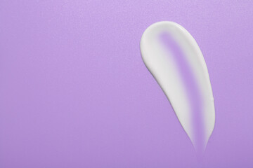 Sample of face cream on violet background, top view. Space for text