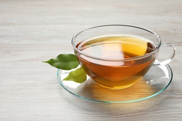 Refreshing green tea in cup and leaves on light wooden table, closeup. Space for text