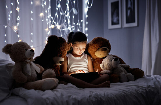 Tablet, digital and kid at night in bed with video, story and youth game with fantasy and learning app. Tech, teddy bear and girl with scroll, relax and evening at home in bedroom on internet