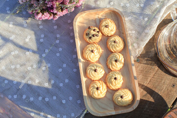 Butter cookie on wooden tray eating coffee under morning sunlight and purple flower on table. Breakfast with nature.