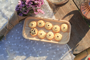 Butter cookie on wooden tray eating coffee under morning sunlight and purple flower on table. Breakfast with nature.