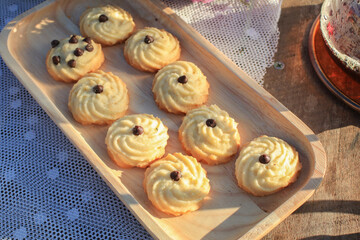 Butter cookie on wooden tray eating coffee under morning sunlight and purple flower on table. Breakfast with nature.