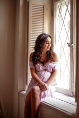 Fototapeta premium Beautiful young woman with curly hair sitting on the window sill.