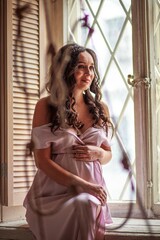 Fototapeta premium Beautiful pregnant woman in white dress near the window. Waiting for a baby concept