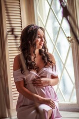 Fototapeta premium Portrait of a beautiful pregnant woman in a pink dress at home