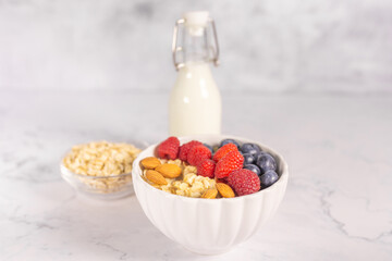 Oatmeal cereal porridge with fresh berries and nuts in white bowl. Healthy breakfast. Dietary. Top view on white marble stone table. 