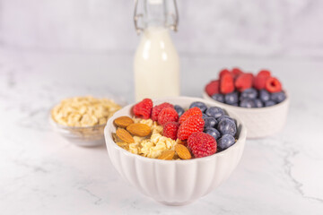 Oatmeal cereal porridge with fresh berries and nuts in white bowl. Healthy breakfast. Dietary. Top view on white marble stone table. 