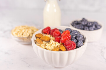 Oatmeal cereal porridge with fresh berries and nuts in white bowl. Healthy breakfast. Dietary. Top view on white marble stone table. 