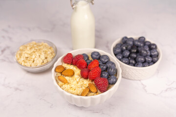 Oatmeal cereal porridge with fresh berries and nuts in white bowl. Healthy breakfast. Dietary. Top view on white marble stone table. 