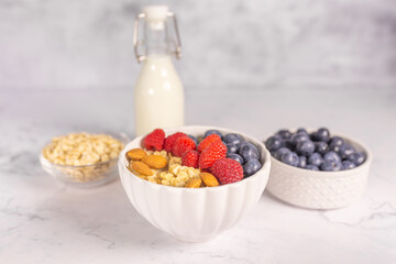 Oatmeal cereal porridge with fresh berries and nuts in white bowl. Healthy breakfast. Dietary. Top view on white marble stone table. 
