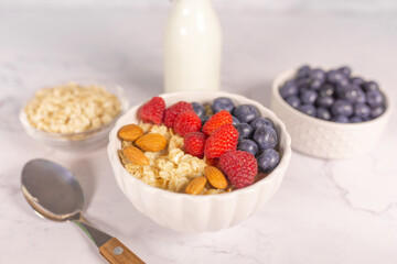 Oatmeal cereal porridge with fresh berries and nuts in white bowl. Healthy breakfast. Dietary. Top view on white marble stone table. 