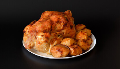 Large round plate with whole baked chicken and new potatoes on a black background.