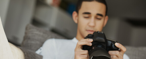 Young photographer setting up dslr camera while sitting on sofa