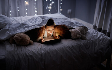 Tablet, reading and kid at night with video, story and youth game with fantasy and language learning app. Tech, teddy bear and young girl with scroll, relax and evening at home in bed on internet