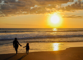 a mother and daughter are walking on the beach at sunset.