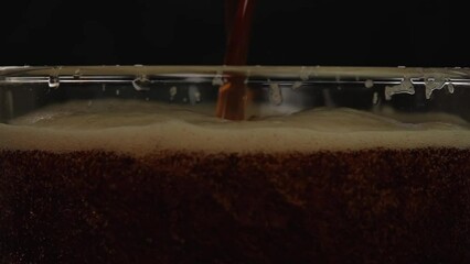 Dark beer is poured into a glass close up. Beer foam in a glass with bubbles slow motion