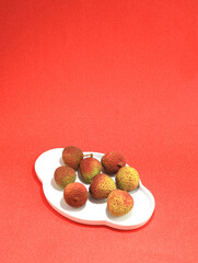 A plate of summer fruit lychees on a red table top