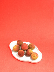 A plate of summer fruit lychees on a red table top