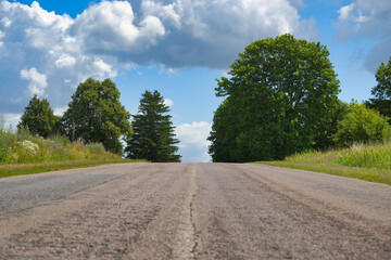 Empty countryside road with lush green trees and blue sky with clouds