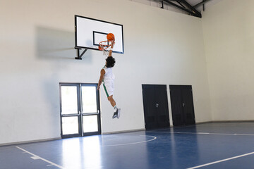 Young biracial man performs a slam dunk in an indoor basketball court