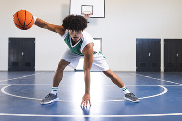 Young biracial man plays basketball indoors, with copy space