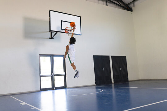Young biracial man performs a slam dunk in an indoor basketball court