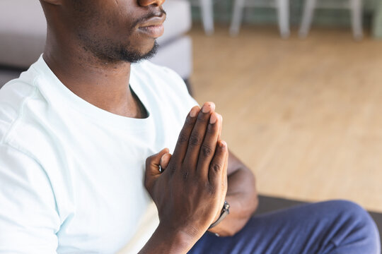 Midsection of african american man with hands in prayer pose practicing yoga meditation at home