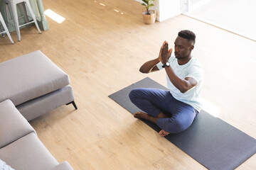 African american man with eyes closed practicing yoga meditation on floor at home, copy space