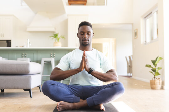 African american man with hands in prayer pose practicing yoga meditation sitting on floor at home